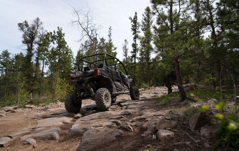 Side-by-side UTV climbing a rocky trail through Colorado trees
